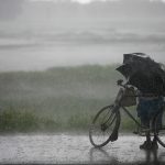 A man on a cycle under an umbrella as it rains in Kerala
