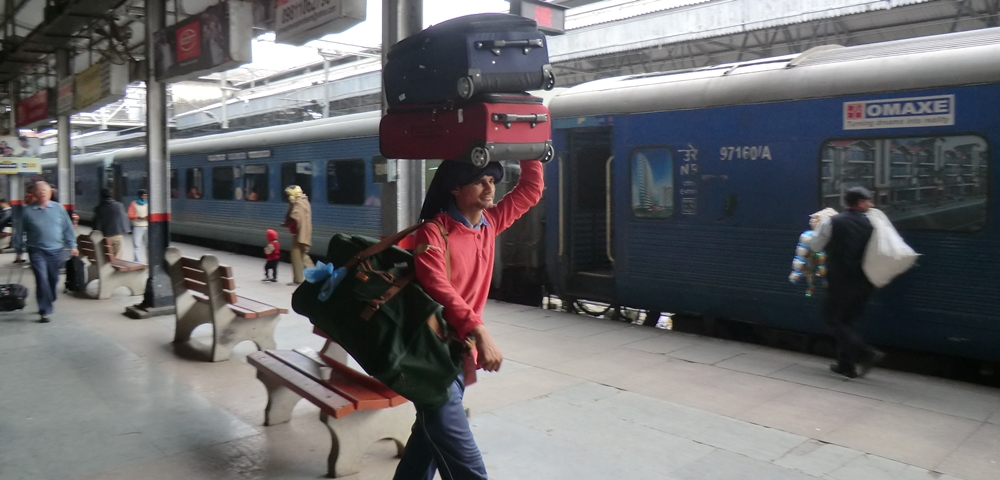 A porter carry three suitcases at a railway station in India