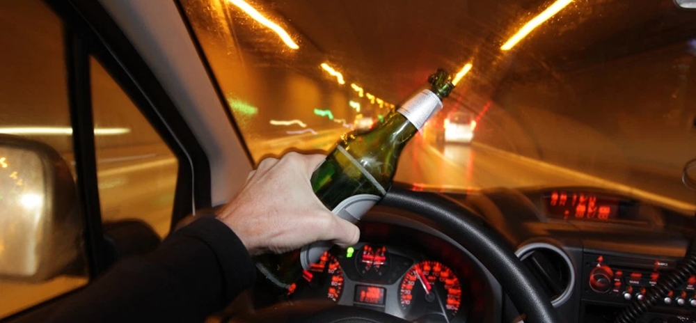 Man holding alcohol bottle while driving