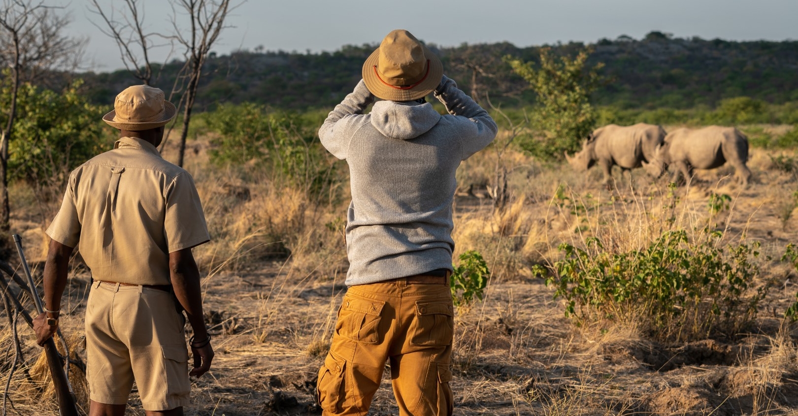 Guide with a gun as a traveler watches rhinoceros 